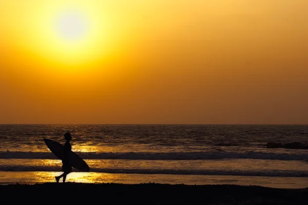 Gün batımında surfboard ile kıyı boyunca bir adam silüeti — Stok fotoğraf