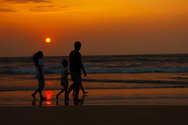 Gün batımında sahil boyunca yürüyerek aile silüeti — Stok fotoğraf