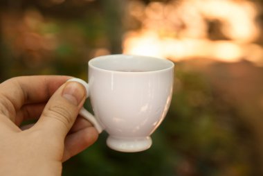 Small cup of tea in hand in nature background clipart