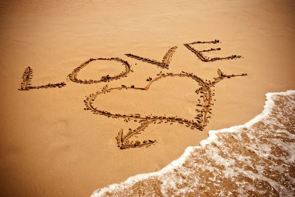 Надпись LOVE and drawing a heart on wet golden beach sand — стоковое фото