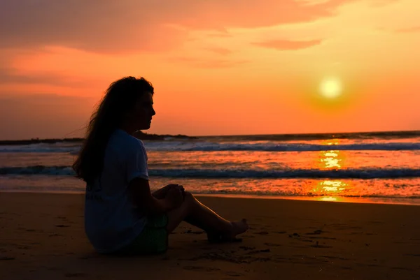 Девушка силуэт от сидит на пляже. Наслаждается спадом — стоковое фото