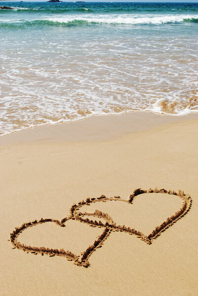 Couple drawing a heart on wet golden beach sand