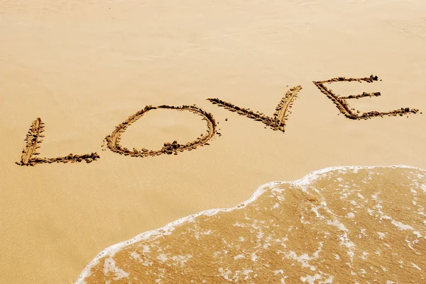 Nápis na písku poblíž moře a vlny - láska. — Stock fotografie