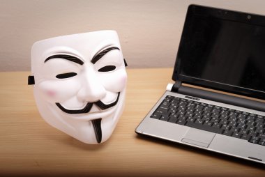 Annonymous maske ve masanın üstünde laptop