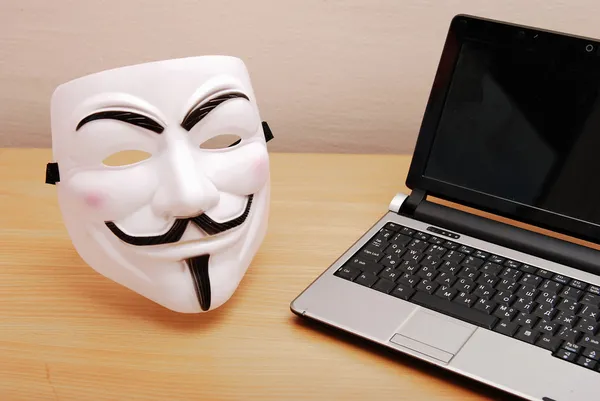 Máscara anônima e laptop na mesa — Fotografia de Stock