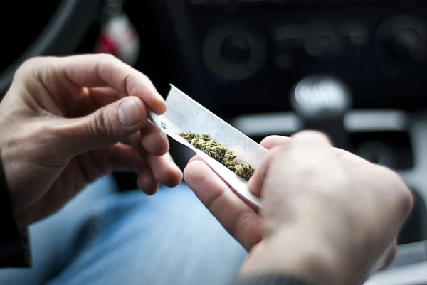 Man making joint and a stash of marijuana in the car — Stock Photo, Image