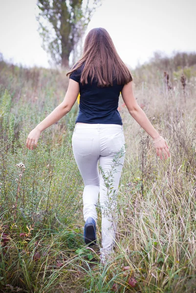 Mladá žena chůze mezi trávy — Stock fotografie