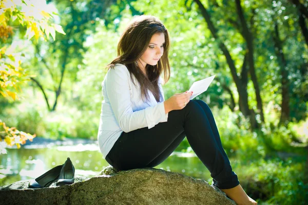 Молодая женщина читает письмо на берегу реки — стоковое фото