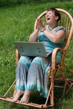 Happy mature woman with laptop in rocking chair handclapping exc clipart