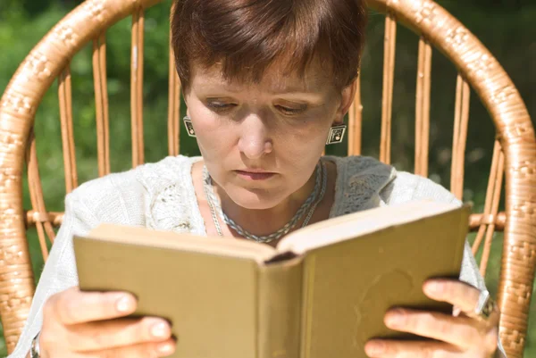 Reife Frau liest Buch im Schaukelstuhl — Stockfoto