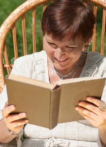 Kitap okuma ve sallanan sandalyede gülerek Olgun kadın — Stok fotoğraf