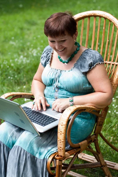 Щаслива зріла жінка з ноутбуком в кріслі для камінгу — стокове фото