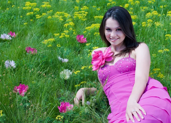Jonge mooie vrouw in roze jurk zittend op groen gras — Stockfoto