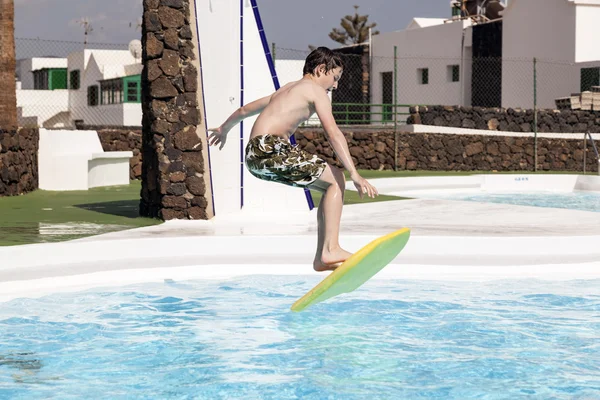 Jongen springen in het zwembad met de surfplank — Stockfoto