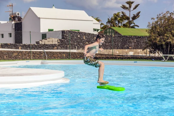 Menino pulando na piscina com a prancha de surf — Fotografia de Stock