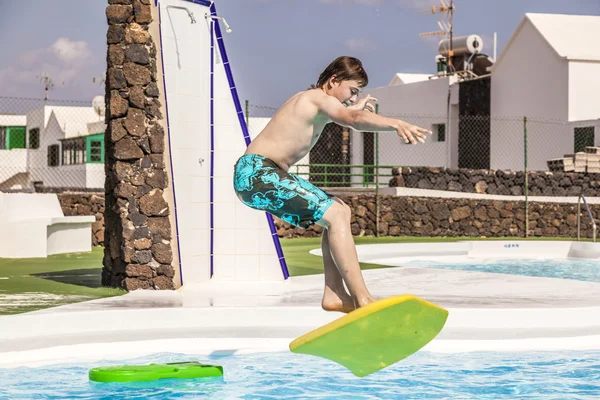 Boy jumping in the pool with the surfboard — Stock Photo, Image