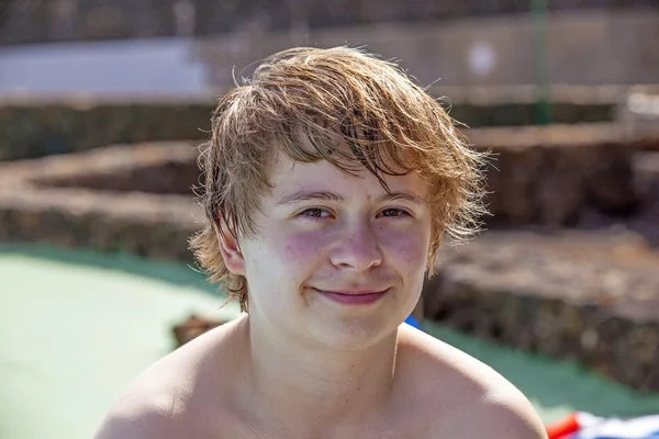 Netter Junge sitzt nach dem Schwimmen im Poolbereich — Stockfoto