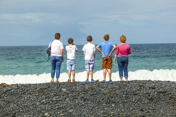 Família observa as ondas na praia vulcânica preta — Fotografia de Stock
