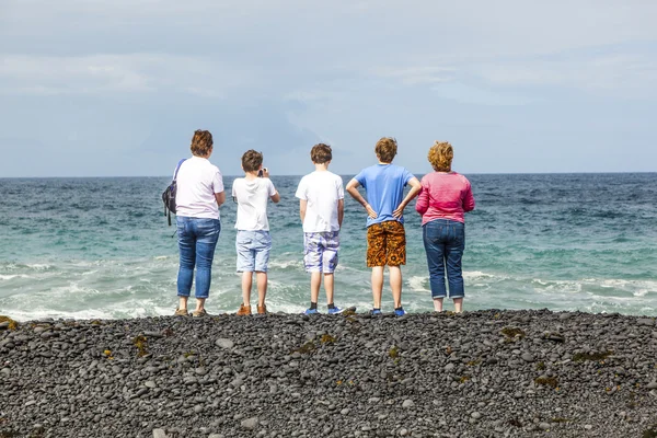 Família observa as ondas na praia vulcânica preta — Fotografia de Stock