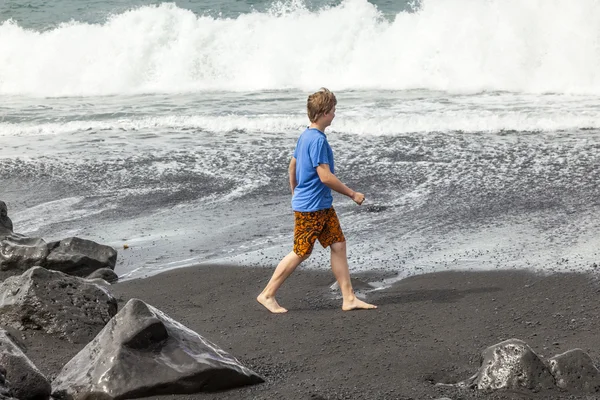 Αγόρι έχει τη διασκέδαση στη μαύρη ηφαιστειακή παραλία — Φωτογραφία Αρχείου