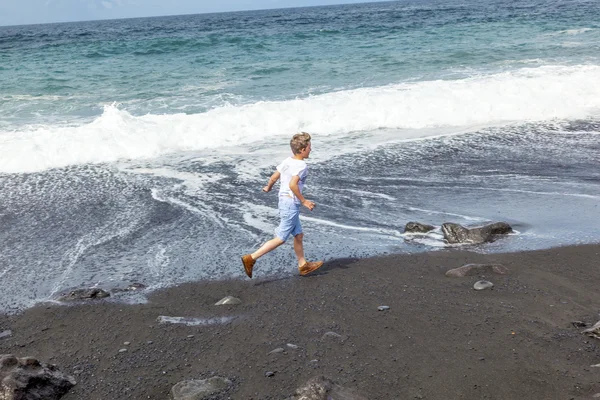 Jongen heeft plezier op het zwarte vulkanische strand — Stockfoto
