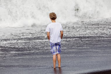 Boy has fun in the spume at the black volcanic beach clipart