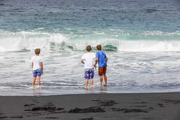Los chicos se divierten en la playa negra volcánica —  Fotos de Stock
