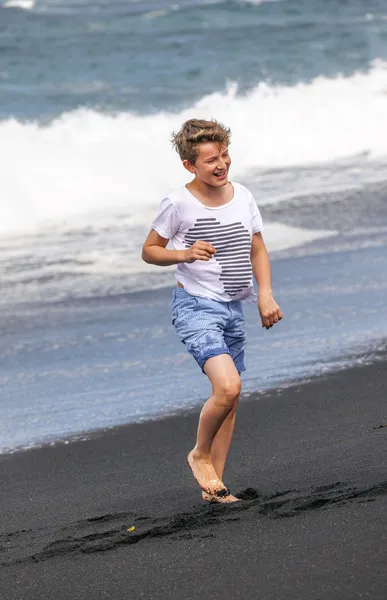 Pojken har kul i spume på den svarta vulkaniska beach — Stockfoto