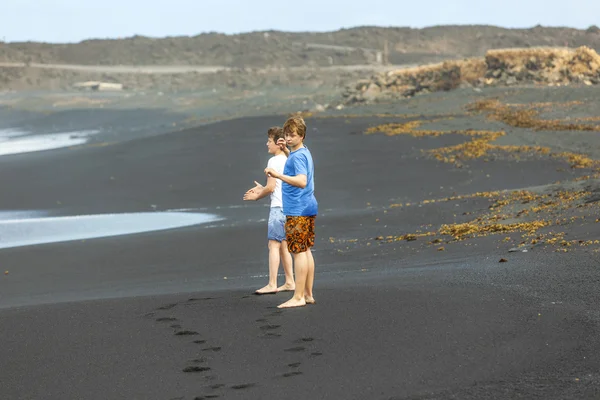 Jongens hebben plezier op het zwarte vulkanische strand — Stockfoto