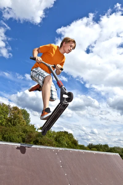 Menino pulando sobre uma rampa com sua scooter — Fotografia de Stock