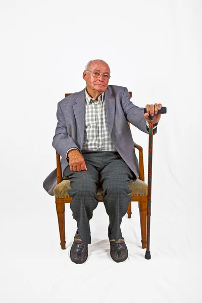 Old friendly man sitting in his armchair with walking stick — Stock Photo, Image