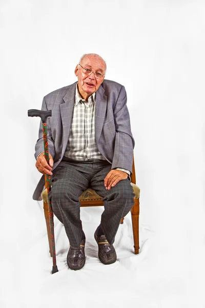 スティックを歩くと彼の肘掛け椅子に座っている古い友好的な人 — ストック写真