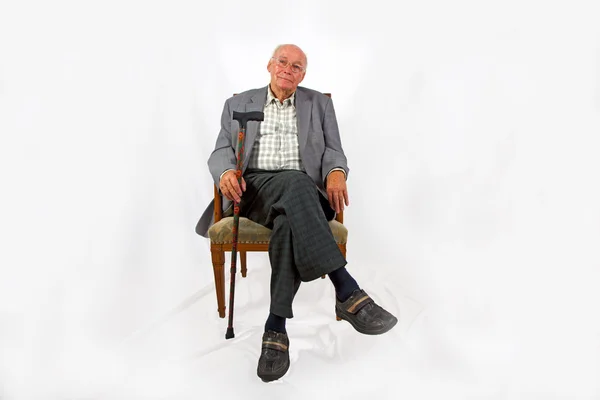 Alter freundlicher Mann sitzt in seinem Sessel mit Gehstock — Stockfoto