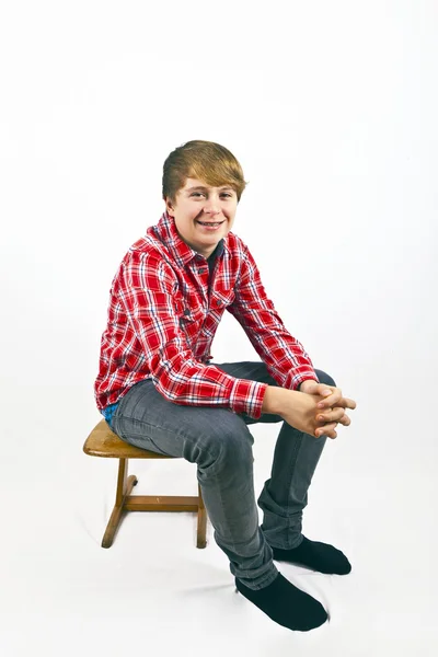 Vänlig ser ung pojke med röd tröja sitter på en trä sc — Stockfoto
