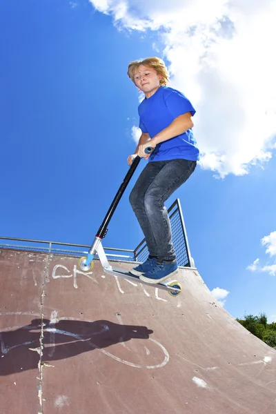 Pojken hoppar med sin skoter över en ramp — Stockfoto