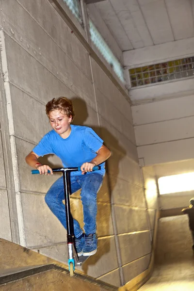 Мальчик прыгает на скутере через рампу в скейтхолле — стоковое фото