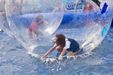 Girls and boys have fun in a huge zorbing ball clipart