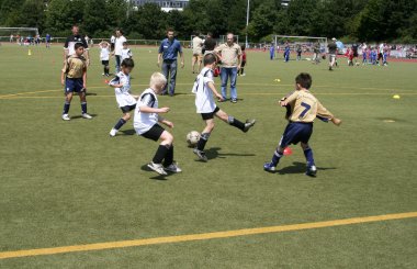 Children playing soccer in summer in an outdoor grass arena clipart