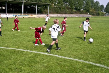 Children playing soccer in summer in an outdoor grass arena clipart