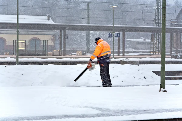 Il lavoratore sta pulendo la piattaforma di una stazione ferroviaria dalla neve — Foto Stock