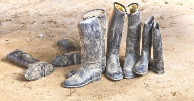 Dirty plastic riding boots standing at the muddy gry ground clipart