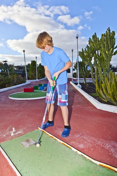 Мальчик играет в мини-гольф на поле — стоковое фото