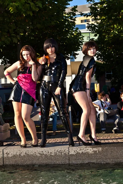 Three girls in black in costumes are posing for photografers — Stock Photo, Image