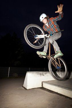 Boy jumping with his bike over a ramp by night clipart