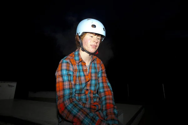 Menino com capacete à noite no parque de skate exausto pela condução — Fotografia de Stock