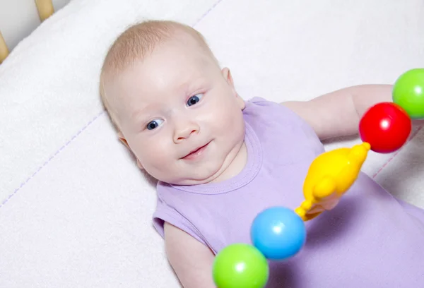 Grijs-eyed baby ligt in bed en spelen speelgoed — Stockfoto
