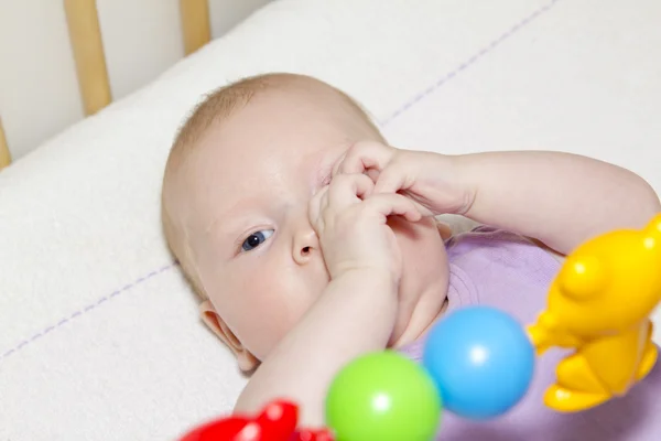El bebé de ojos grises yace en la cama y juega a los juguetes —  Fotos de Stock
