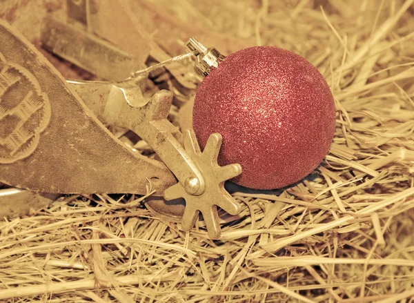 Vaquero de Navidad - espolones viejos en el heno con un adorno de bola roja —  Fotos de Stock