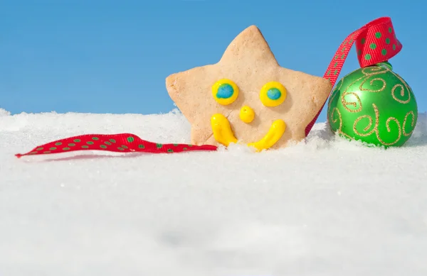 A delightful Christmas cookie on snow with a green Christmas bauble — Stock Photo, Image