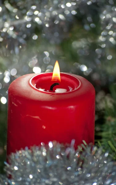 Rote Weihnachtskerze brennt, umgeben von silbrig glänzendem Lametta — Stockfoto